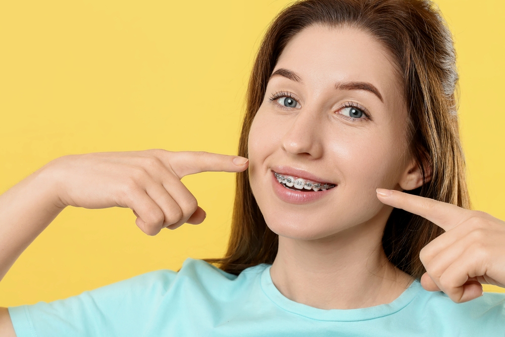 smiling-woman-pointing-her-metal-braces-yellow-background